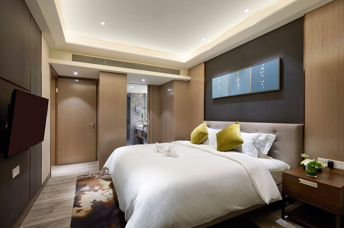 A modern hotel room with a large bed, a flat-screen TV, a bedside table, and a wall-mounted artwork.