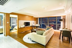 A modern hotel room with a living area, a dining table, a sofa, and a TV.