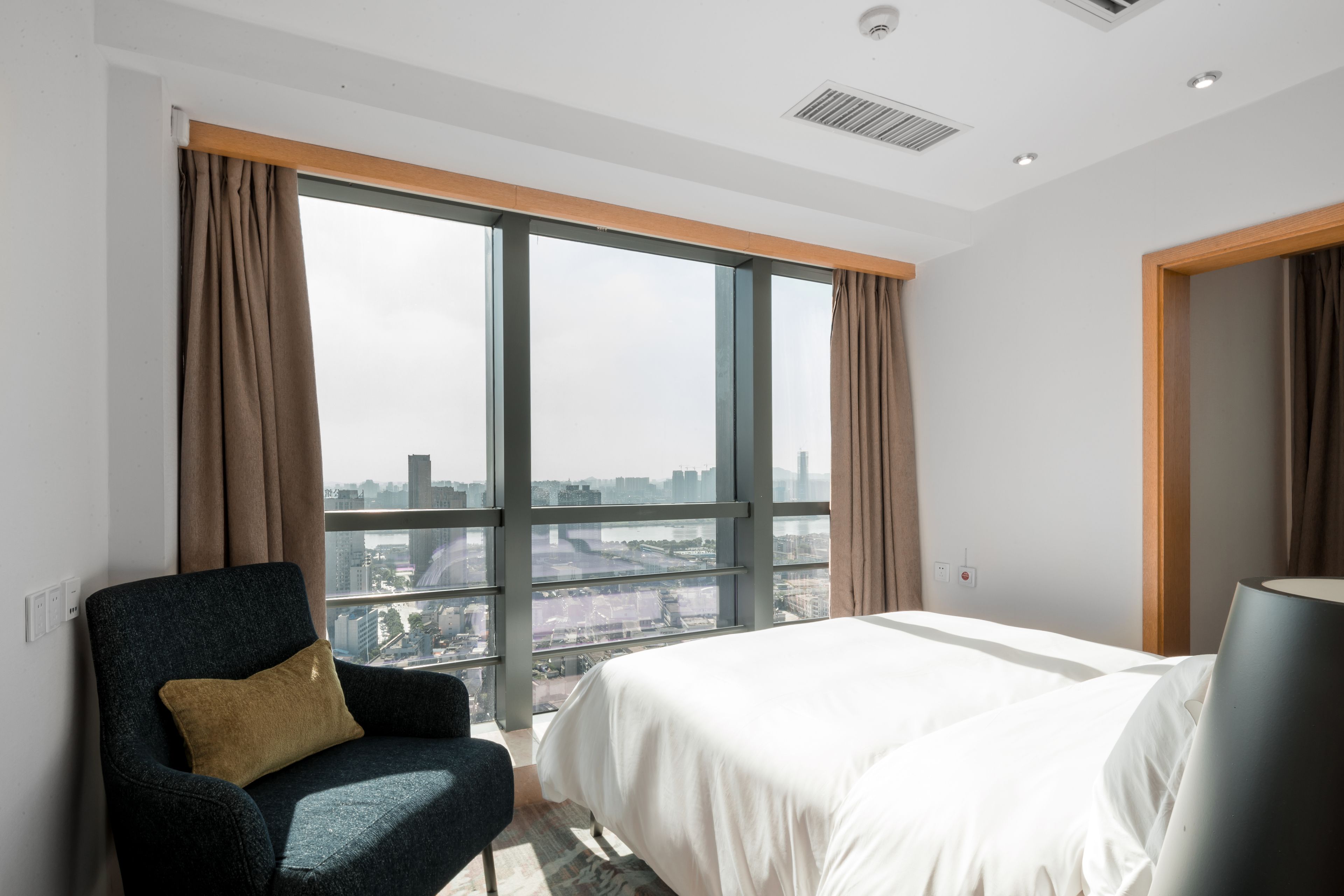 Een hotelkamer met een groot raam, een bed, een stoel en een lamp.