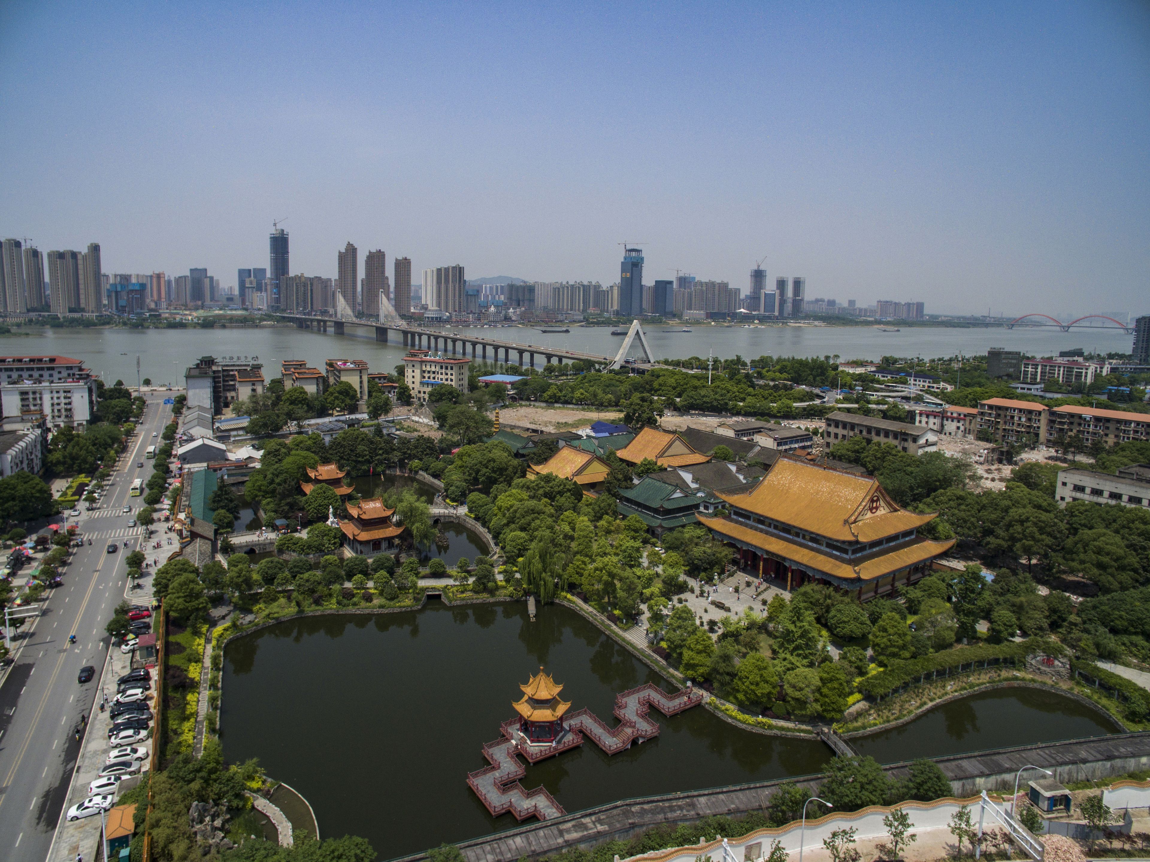 Un parque junto al río con arquitectura tradicional, un puente y un horizonte urbano al fondo.