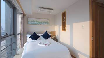 Habitación de hotel con una cama grande, vistas de la ciudad a través de una ventana, un cuadro en la pared y una estantería de madera con una botella.