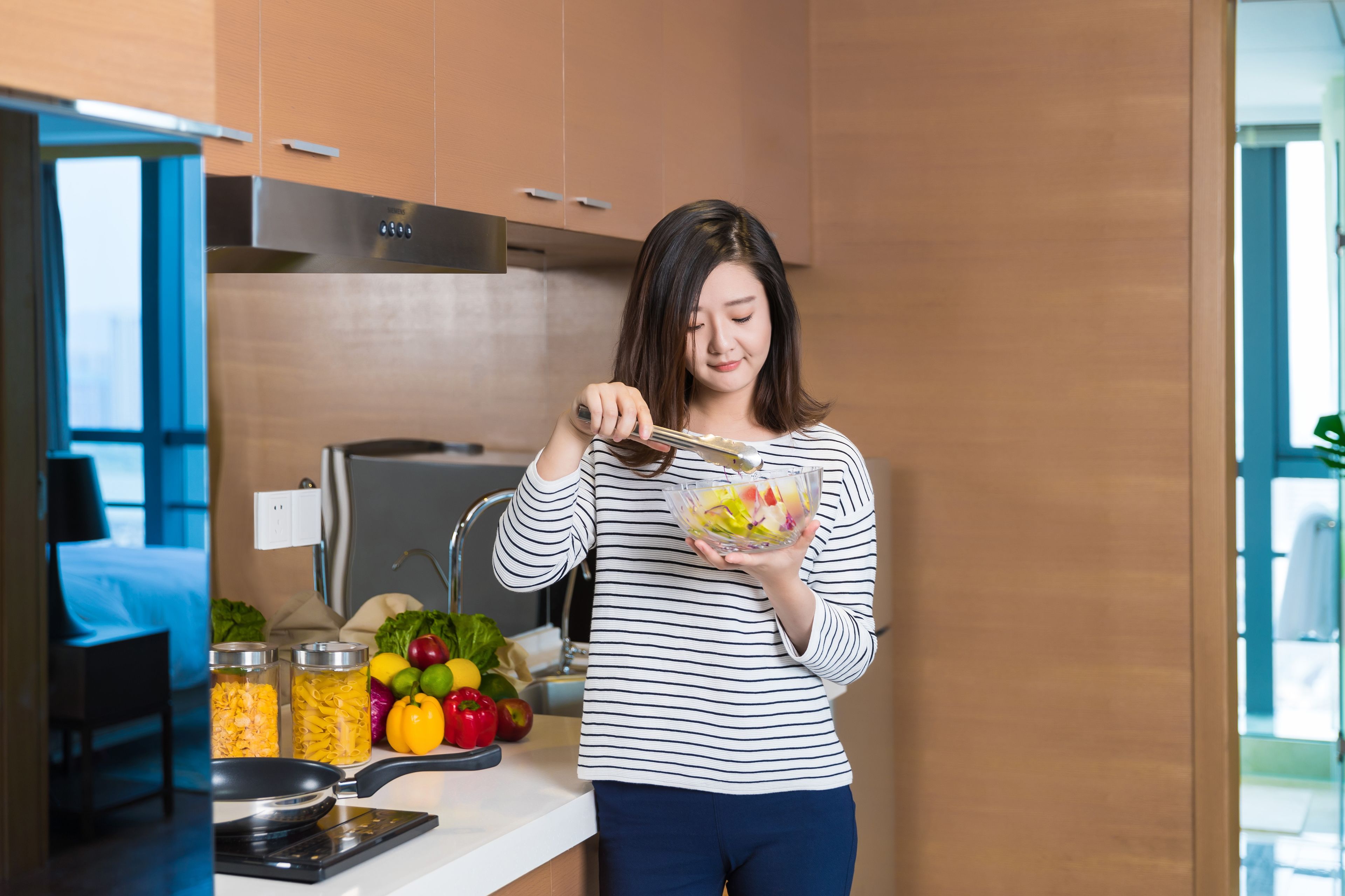 A modern kitchen with stainless steel appliances, a countertop with jars of food, and a variety of fresh produce.