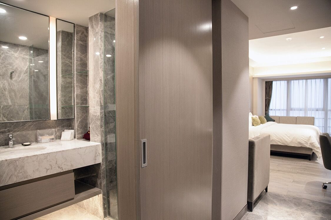 Een moderne hotelkamer met een marmeren badkamer, een groot bed en uitzicht op de stad.