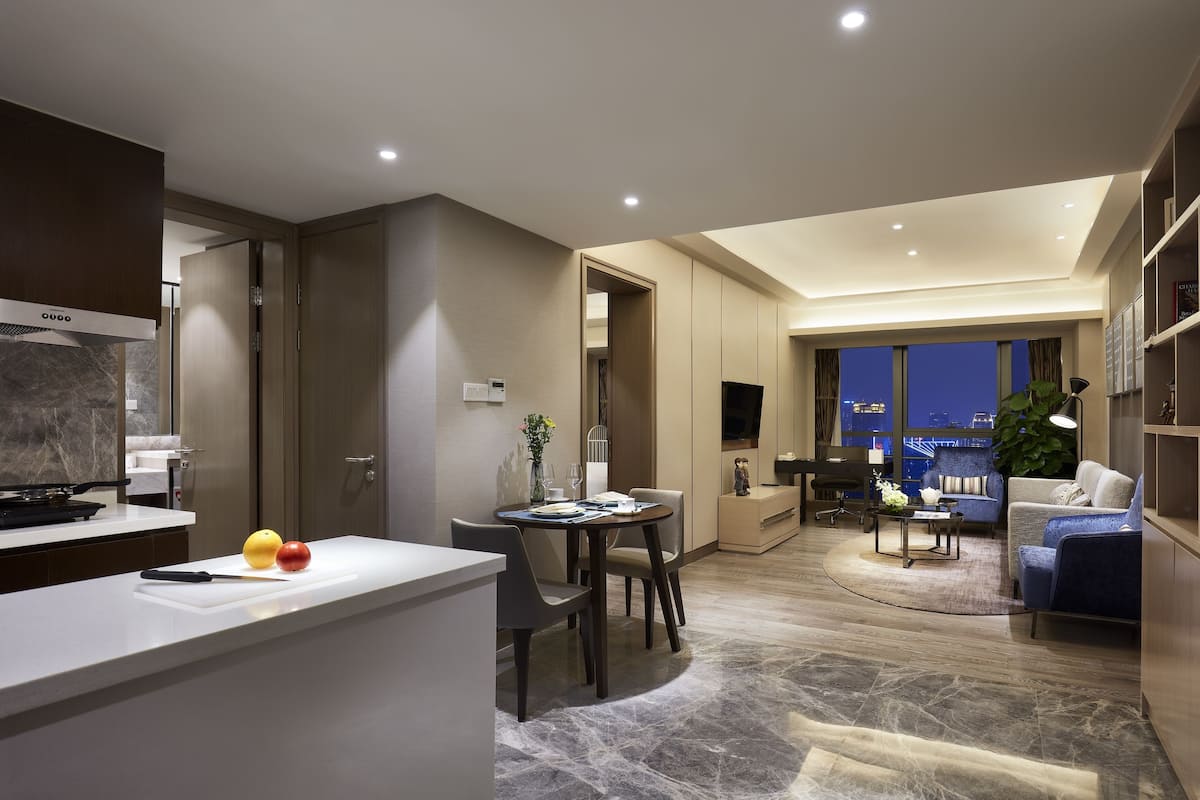 Eine moderne Küche mit Essbereich, ein Wohnzimmer mit Sofa und Fernseher sowie ein Blick auf die Stadt durch große Fenster.