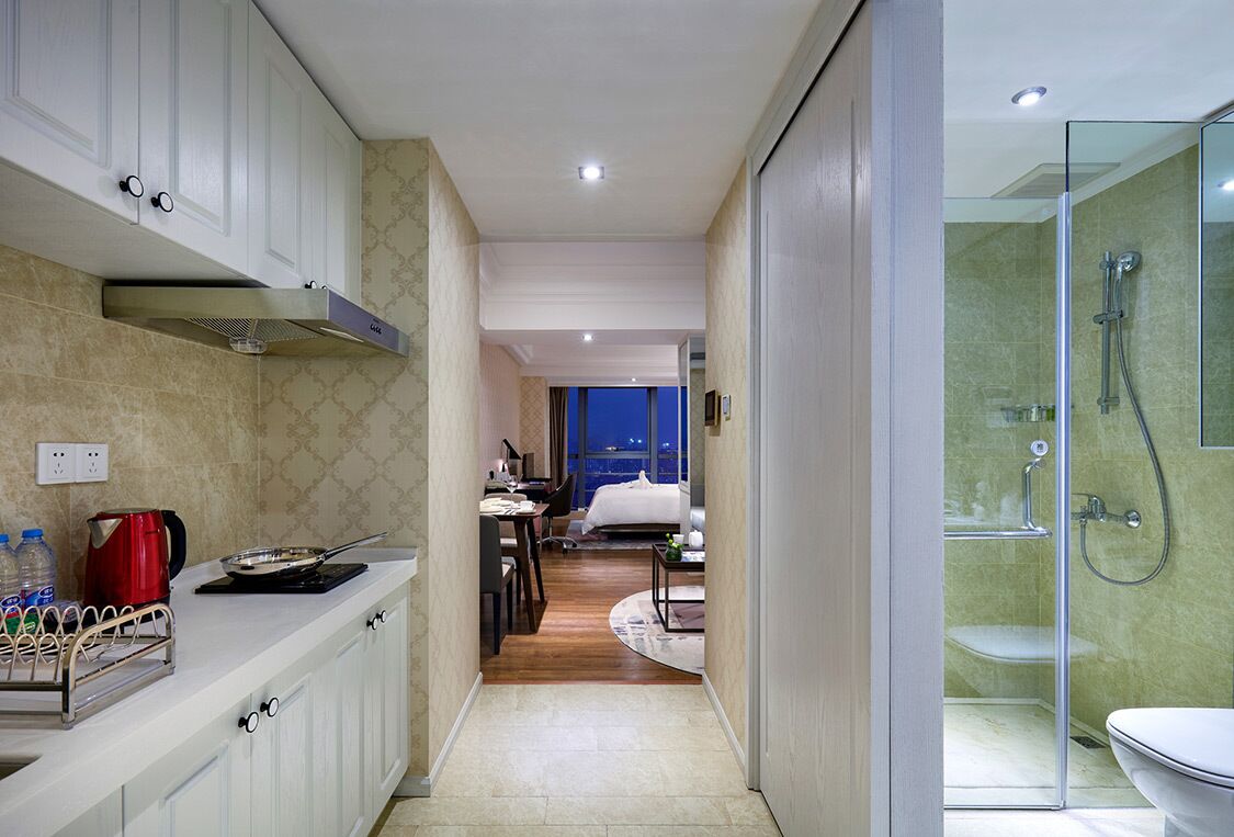 Una habitación de hotel moderna con cocina, un dormitorio separado y ducha con cerramiento de vidrio.