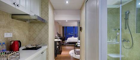 Una habitación de hotel moderna con cocina, un dormitorio separado y ducha con cerramiento de vidrio.