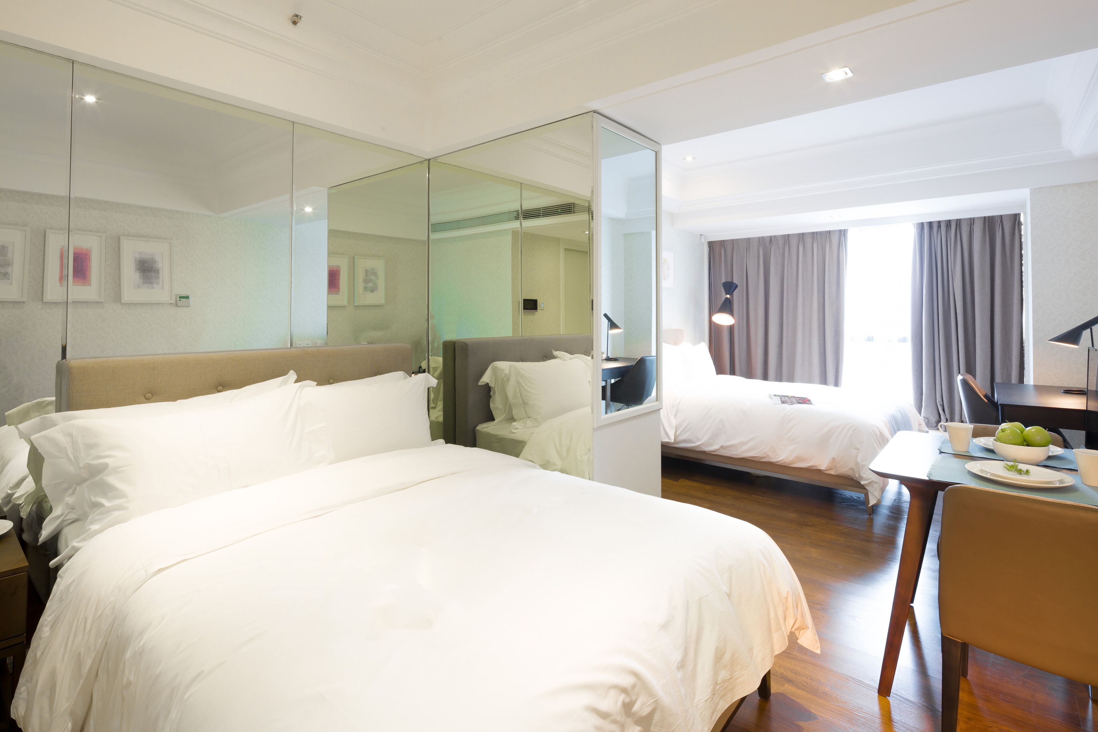 Een hotelkamer met twee bedden, een zithoek en een spiegel die de kamer weerspiegelt.