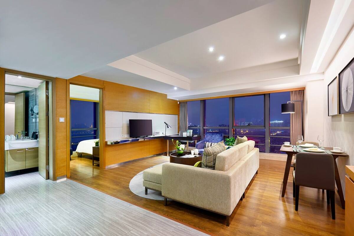 Ein modernes Hotelzimmer mit Wohnbereich, Essbereich und großem Fenster mit Blick auf die Stadt.