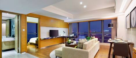 A modern hotel room with a living area, a dining space, and a large window with a city view.