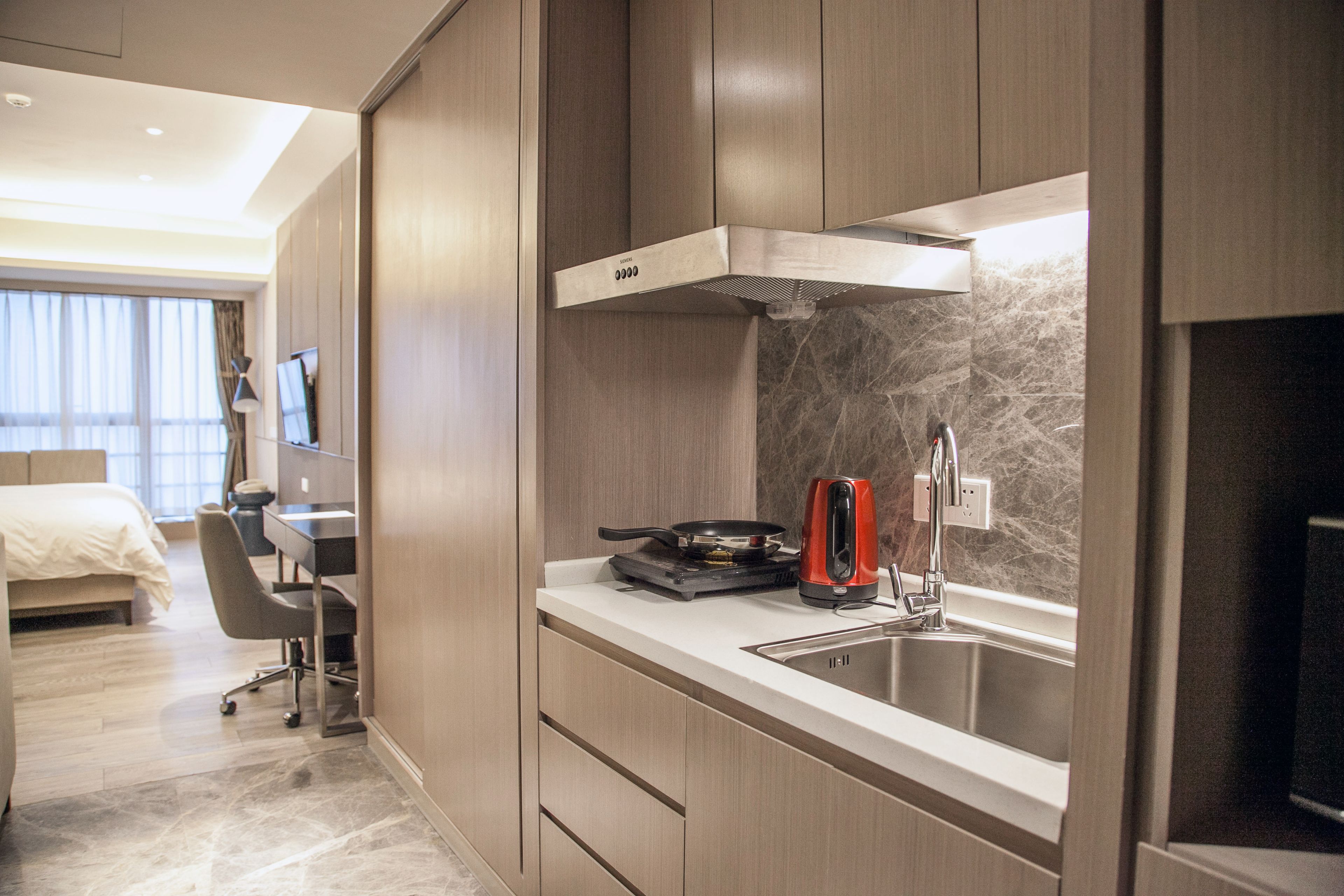 Una habitación de hotel moderna con kitchenette, cama, escritorio y televisor.