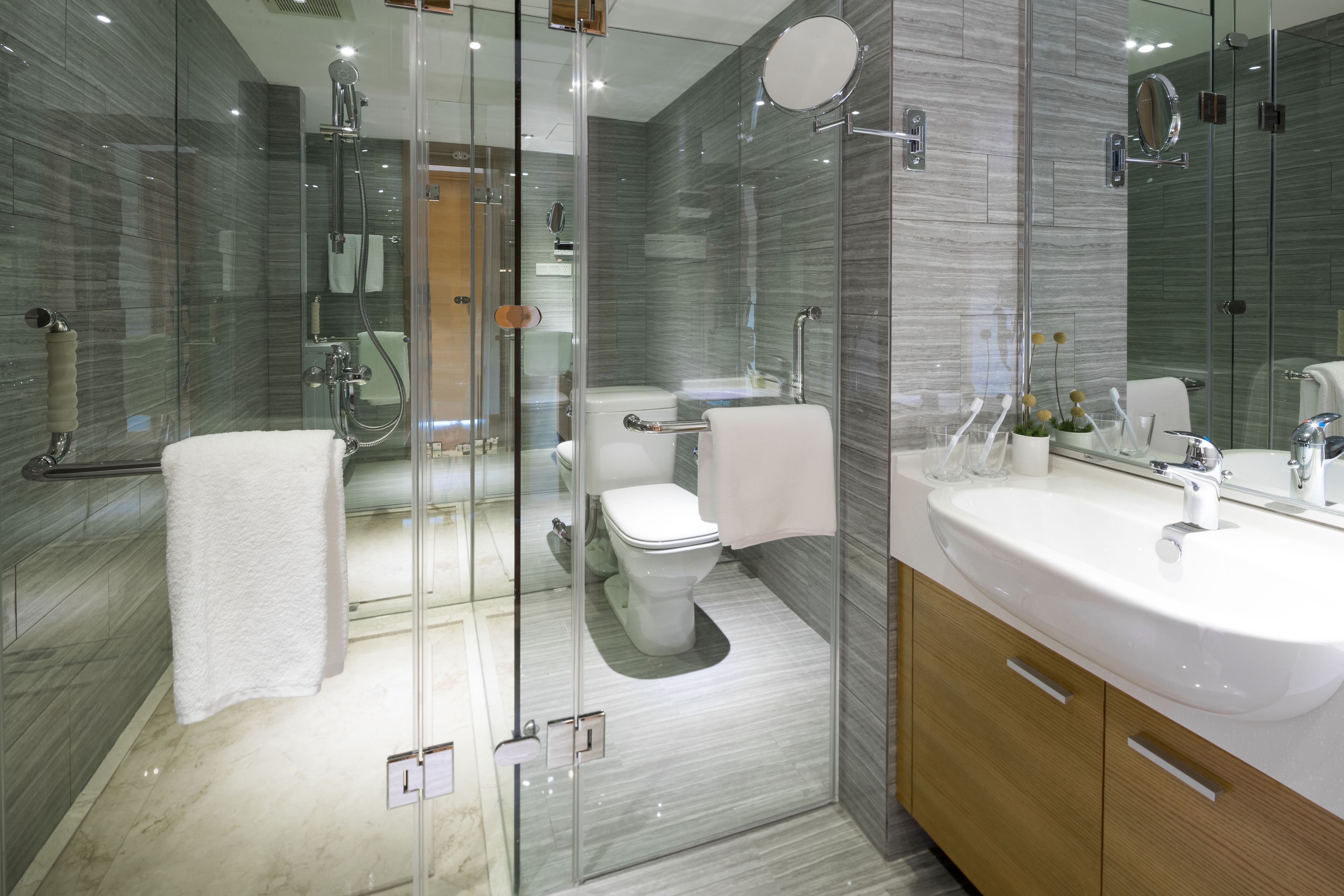 A modern bathroom with a glass-enclosed shower, a white toilet, and a large vanity with a sink and mirror.