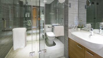 A modern bathroom with a glass-enclosed shower, a white toilet, and a large vanity with a sink and mirror.