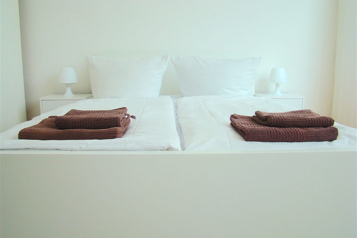 A double bed with white linens and two brown towels folded on each side.