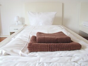 Una cama bien hecha con sábanas blancas y un edredón marrón doblado al pie.