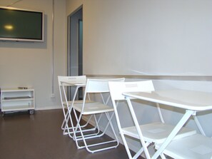 Ein Klassenzimmer mit weißen, zusammenklappbaren Tischen und Stühlen, einer Tafel und einem Tablelständer.