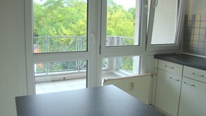 Cuina amb armaris blancs, un taulell gris i vista a un balcó amb barana.