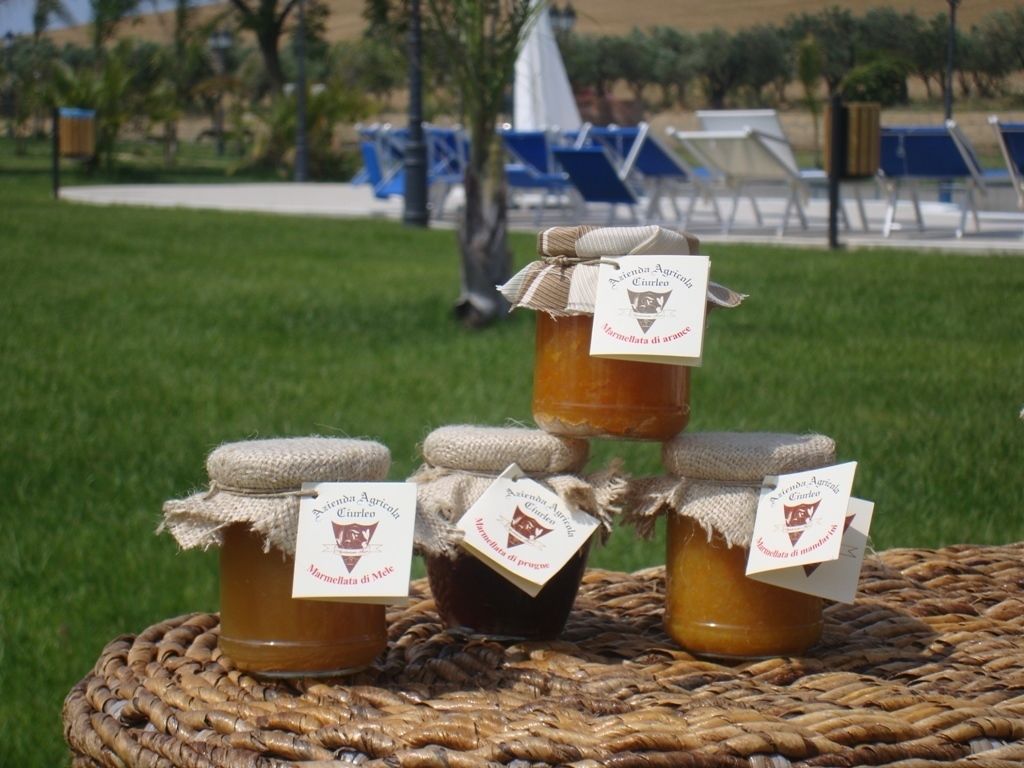 Tres tarros de miel sobre una estera tejida, con etiquetas, frente a un área verde y sillones de descanso.