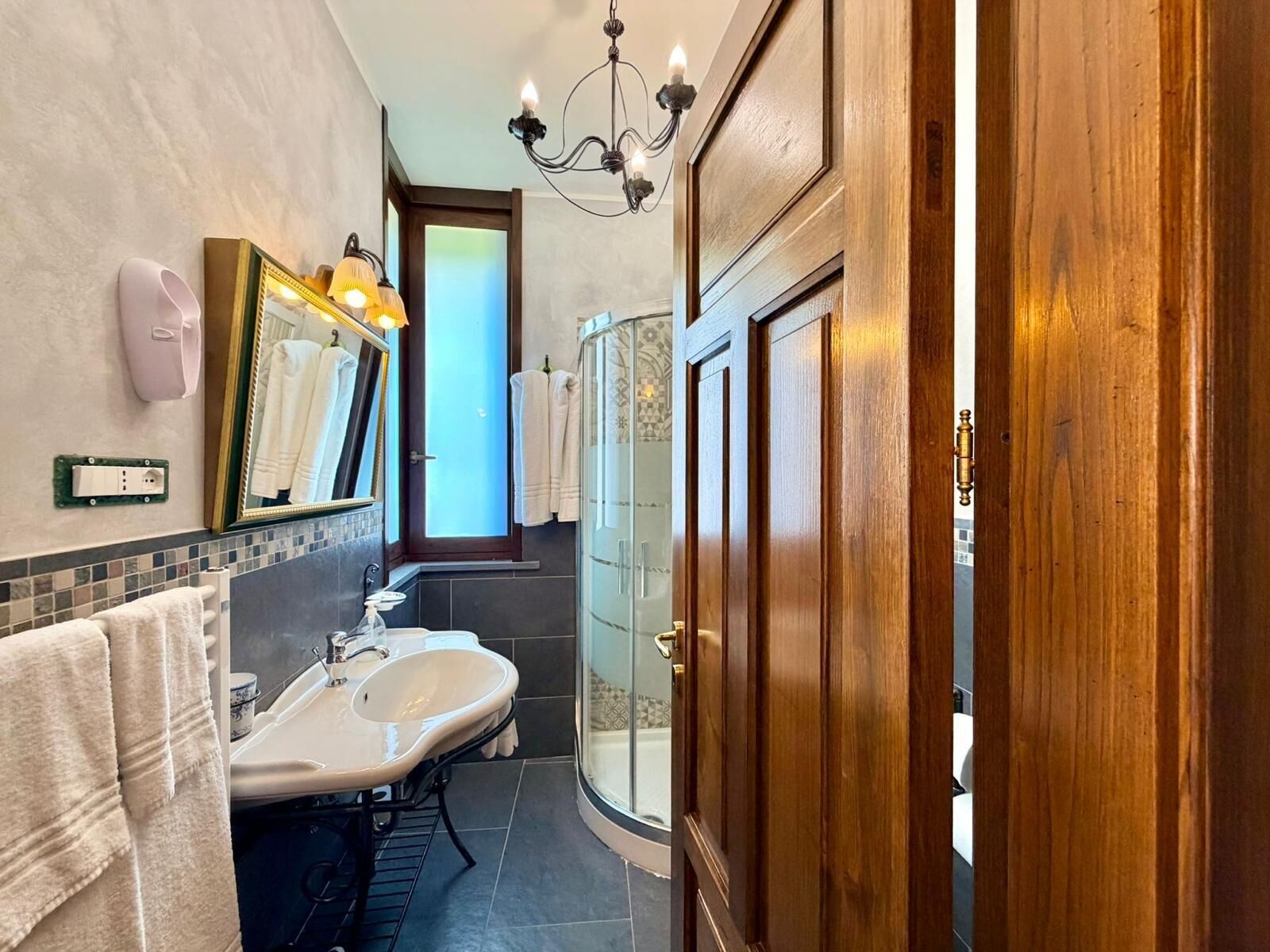 A bathroom with a sink, mirror, towel rack, shower, and a chandelier.