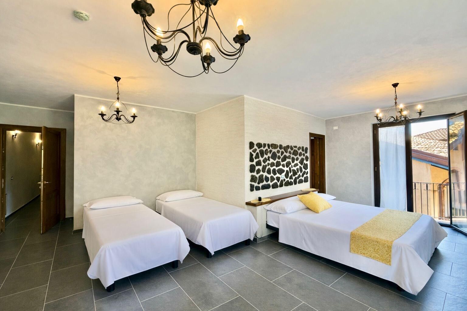 A hotel room with two single beds, a large window, a chandelier, and a stone wall decoration.