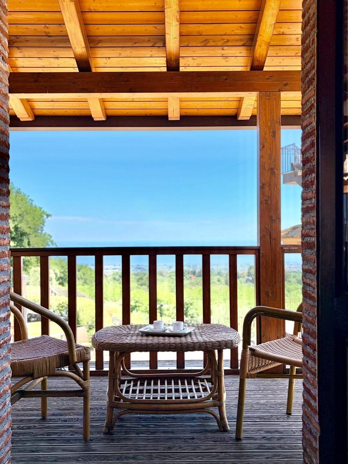 A wooden deck with wicker furniture and a table, overlooking a scenic view.