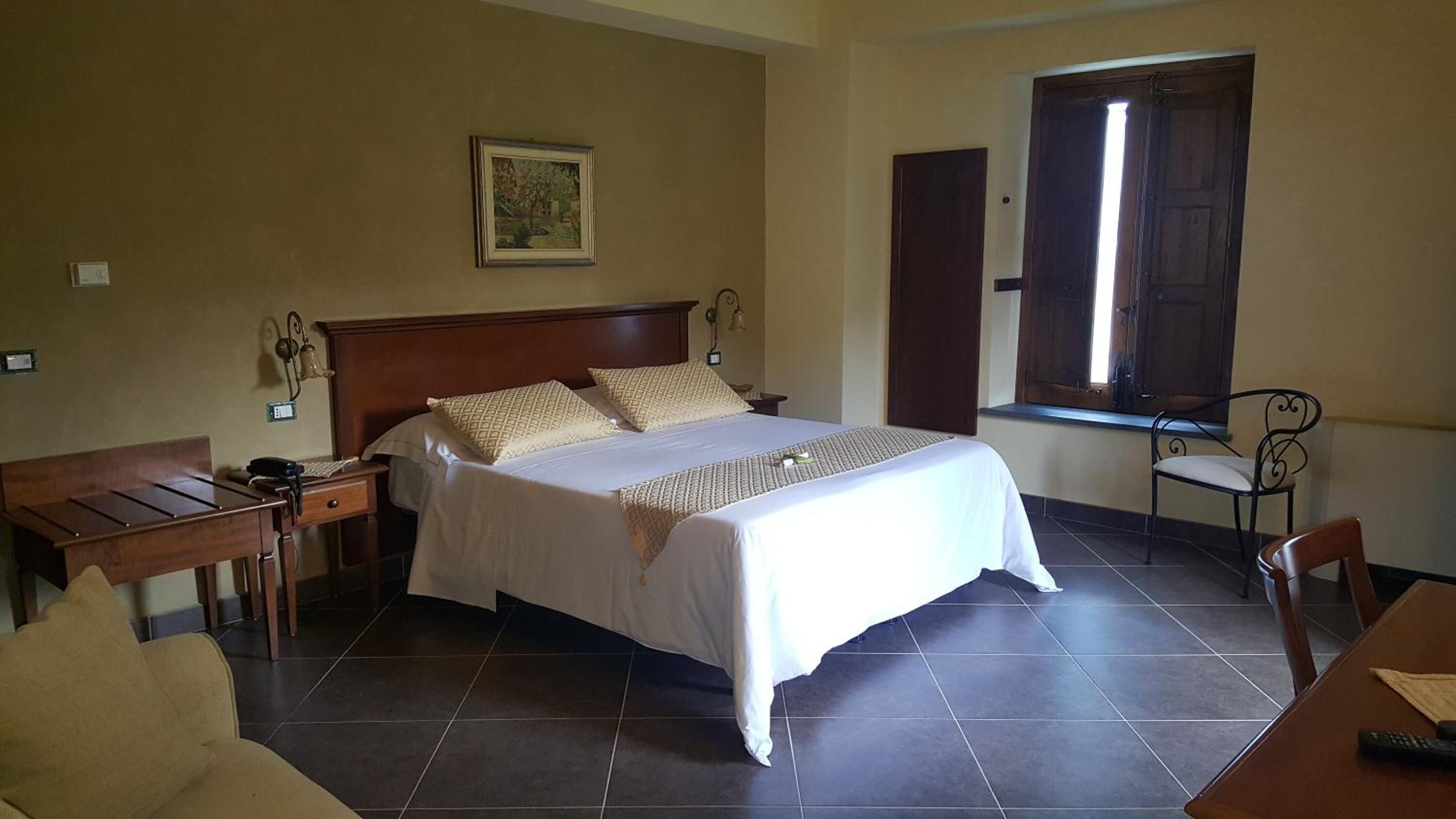 A hotel room with a bed, bedside tables, a desk, a chair, and a window.