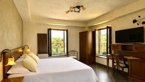 Habitación de hotel con cama, escritorio, silla, televisión y ventanas amplias.