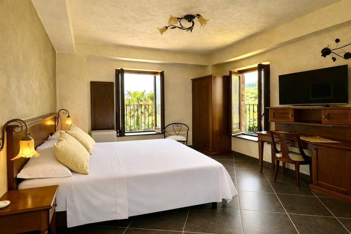 A hotel room with a bed, a desk, a chair, a television, and large windows.