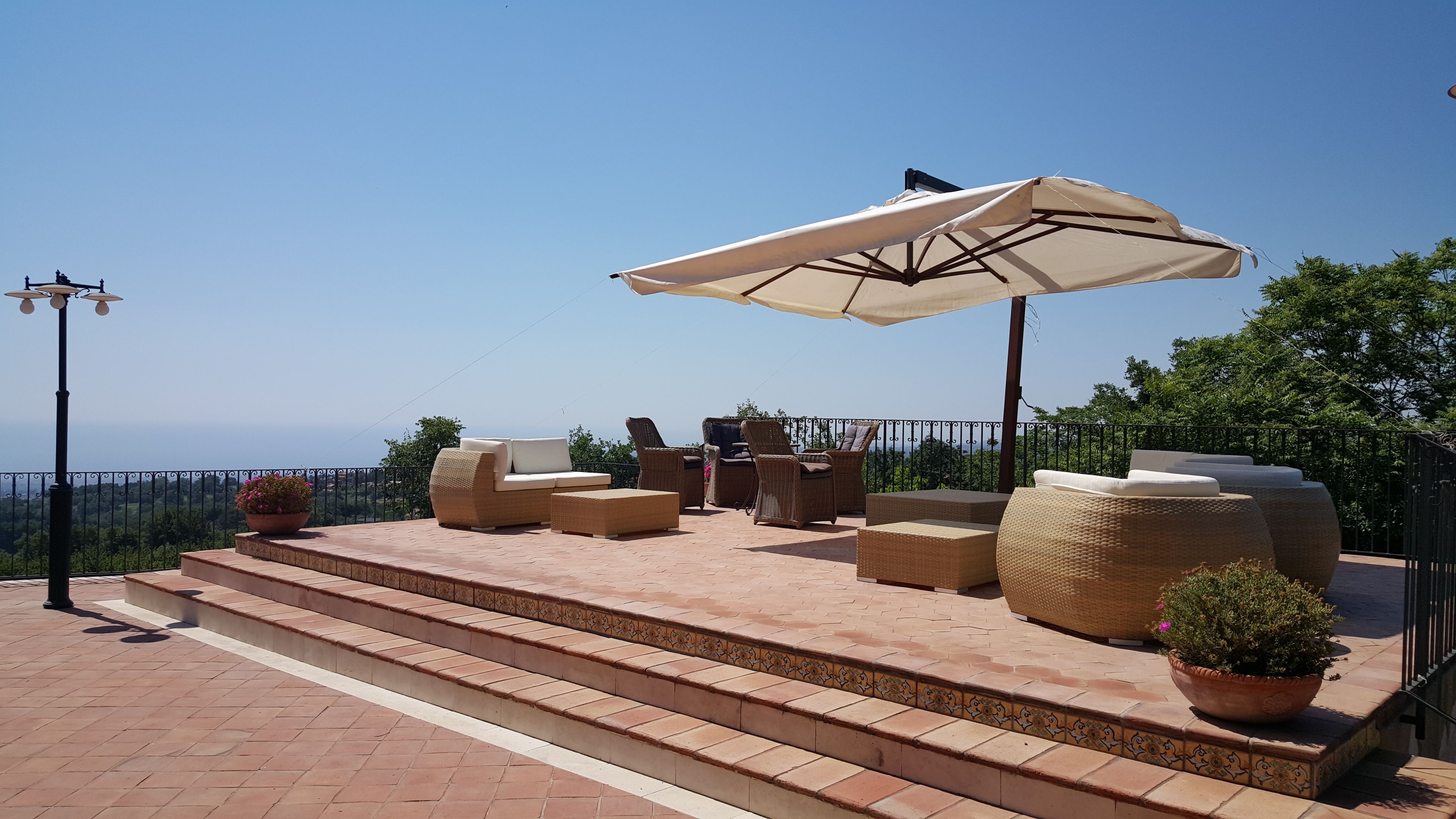 A terrace with wicker furniture, a large umbrella, and potted plants.
