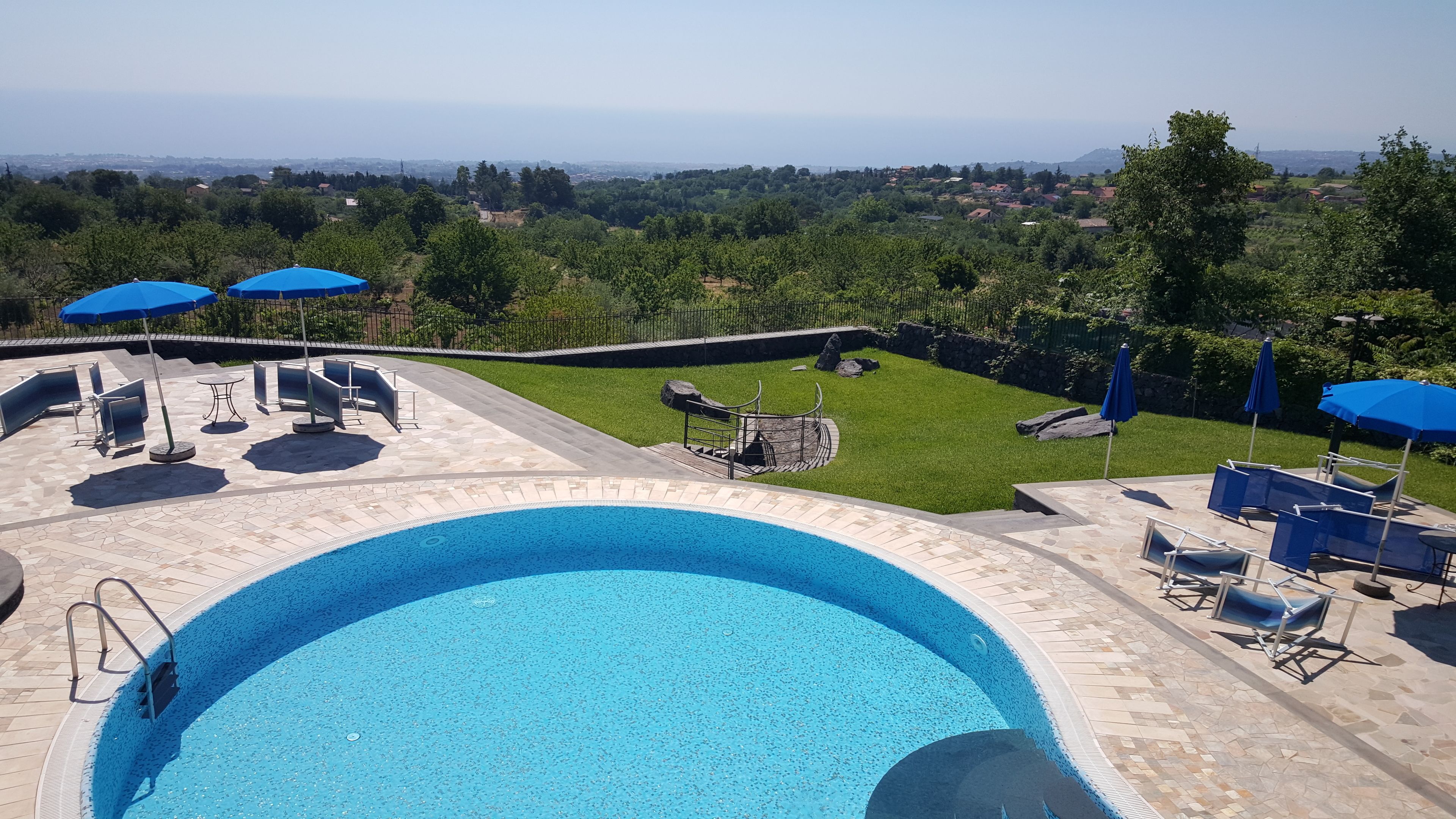 A swimming pool with lounge chairs and umbrellas, surrounded by a stone deck and a view of a green landscape.