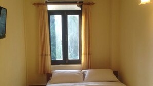 Una habitación de hotel con cama, cortinas, ventana y un equipo de aire acondicionado.