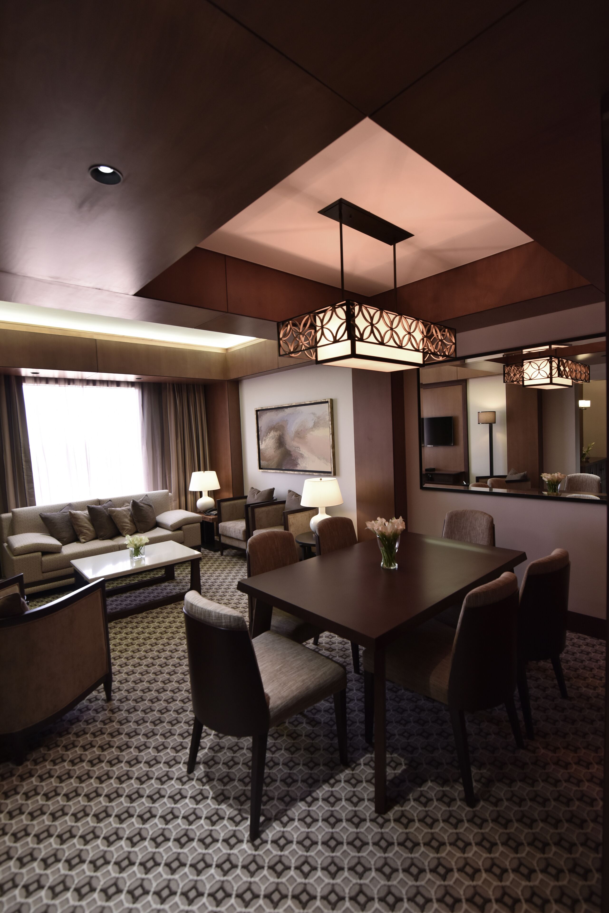 Une chambre d’hôtel comprenant un coin repas, un canapé, une télévision et un grand miroir.