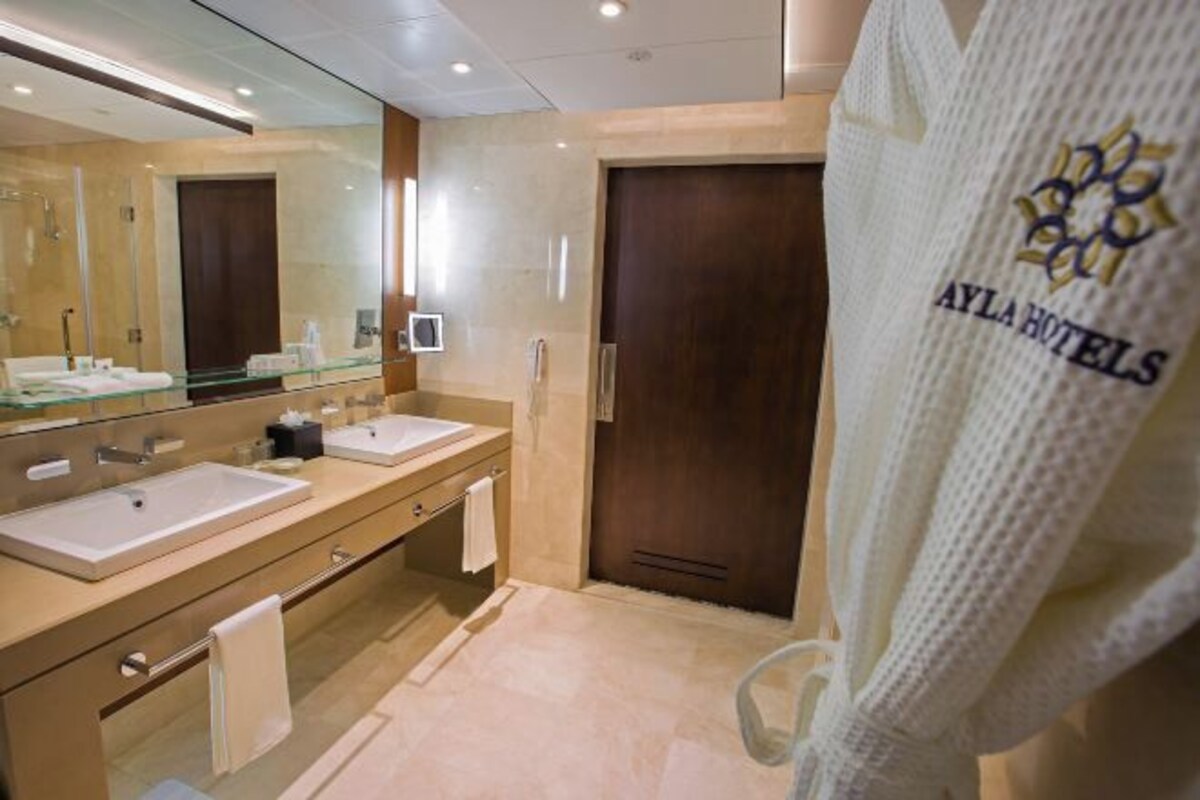 A modern bathroom with two sinks, a large mirror, and a robe hanging on a hook.