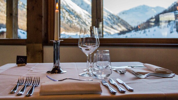 Une table dressée avec des couverts et des verres, une bougie, et une vue sur les montagnes par la fenêtre.