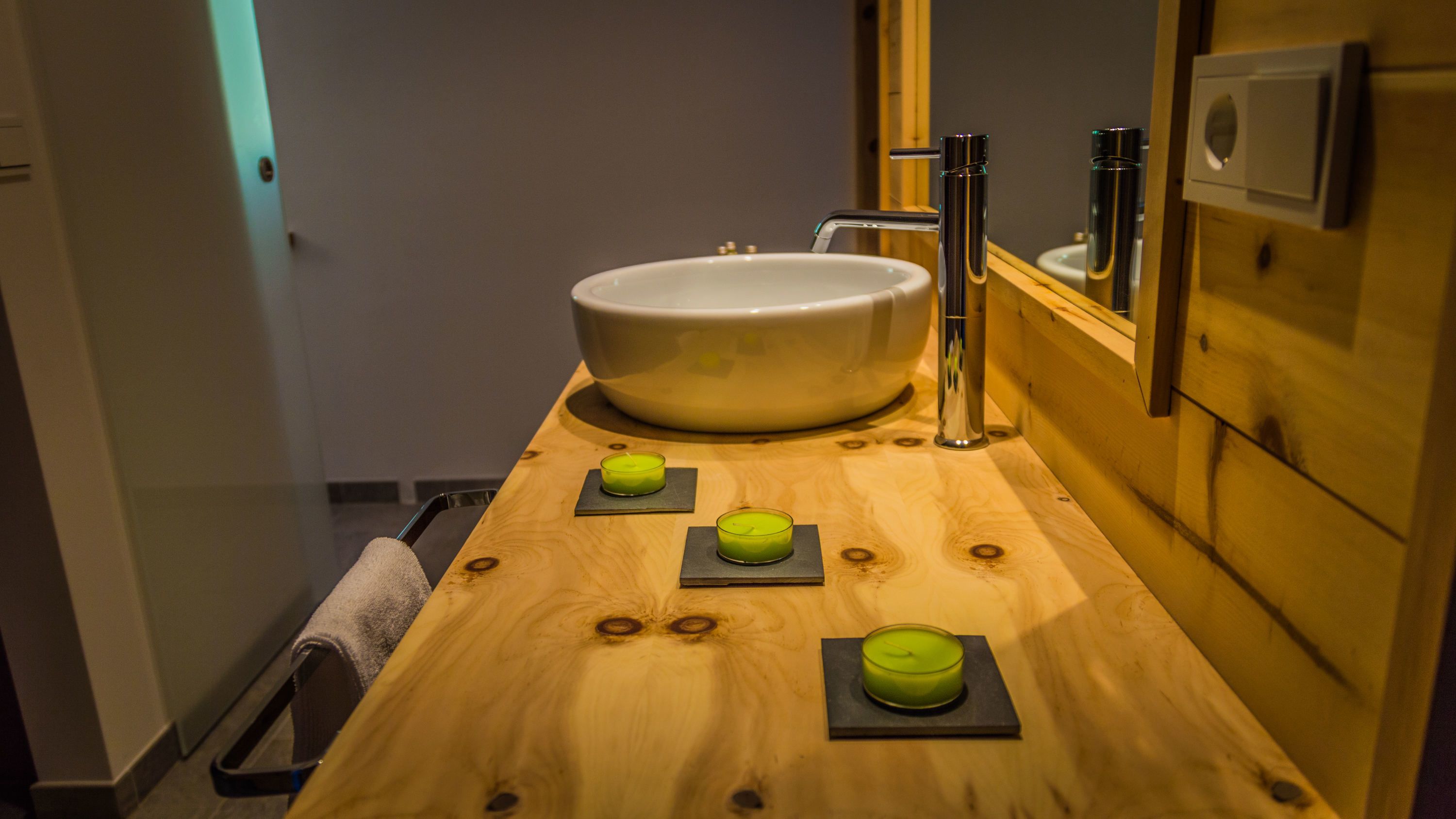 Une salle de bain avec un meuble-lavabo en bois, un grand évier et trois bougies vertes posées sur des supports noirs.