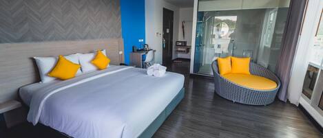 A modern hotel room with a large bed, a seating area, and a glass door leading to a balcony.