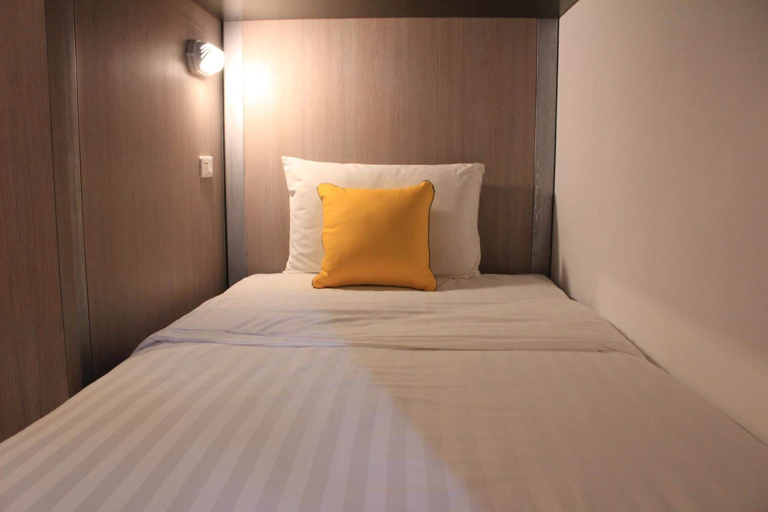 A small, single-bed room with a wooden headboard, a white pillow, and a yellow accent pillow.