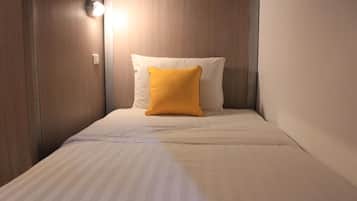 A small, single-bed room with a wooden headboard, a white pillow, and a yellow accent pillow.