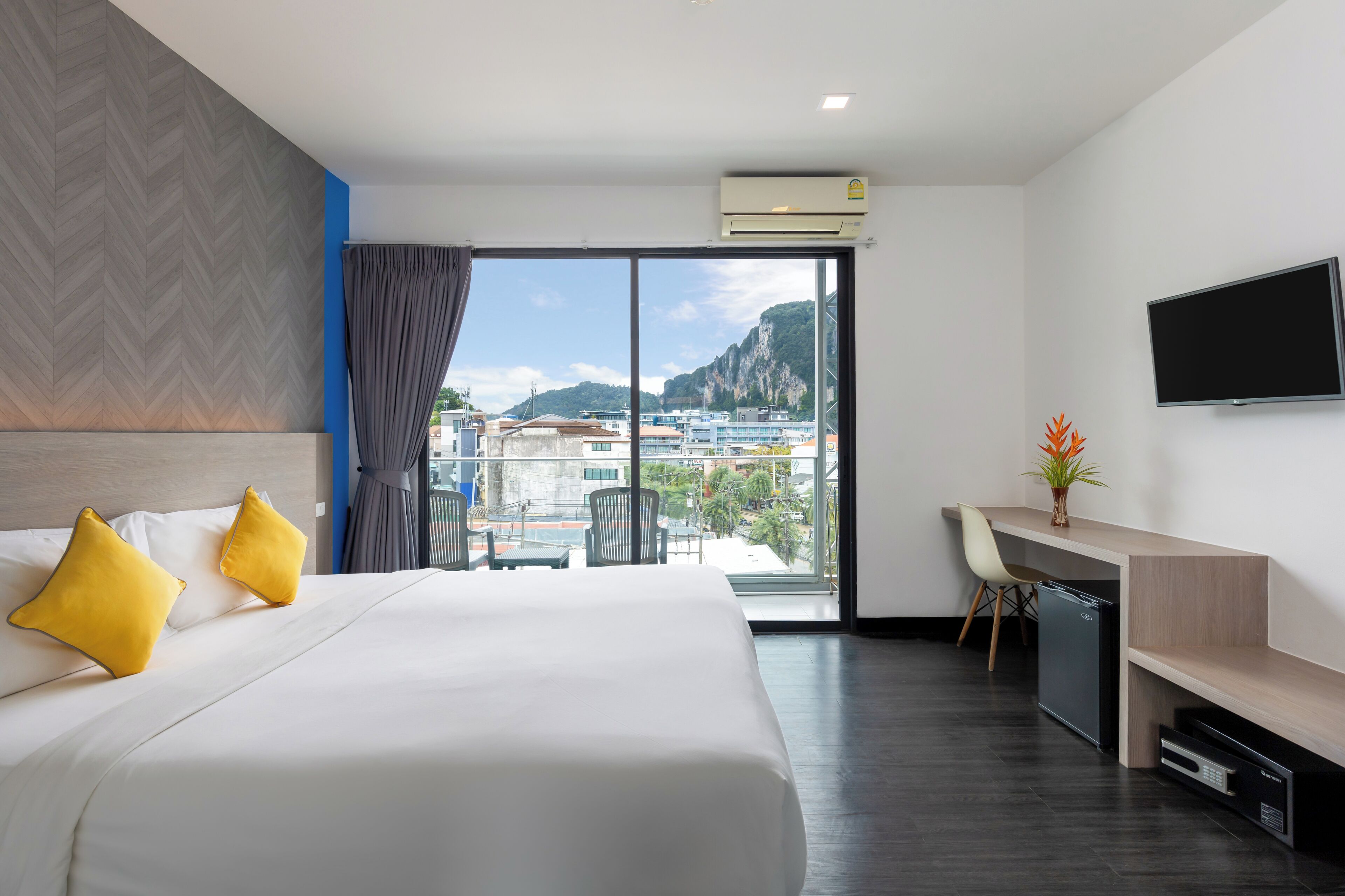 A hotel room with a bed, a desk, a chair, a TV, and a view of the city and mountains.