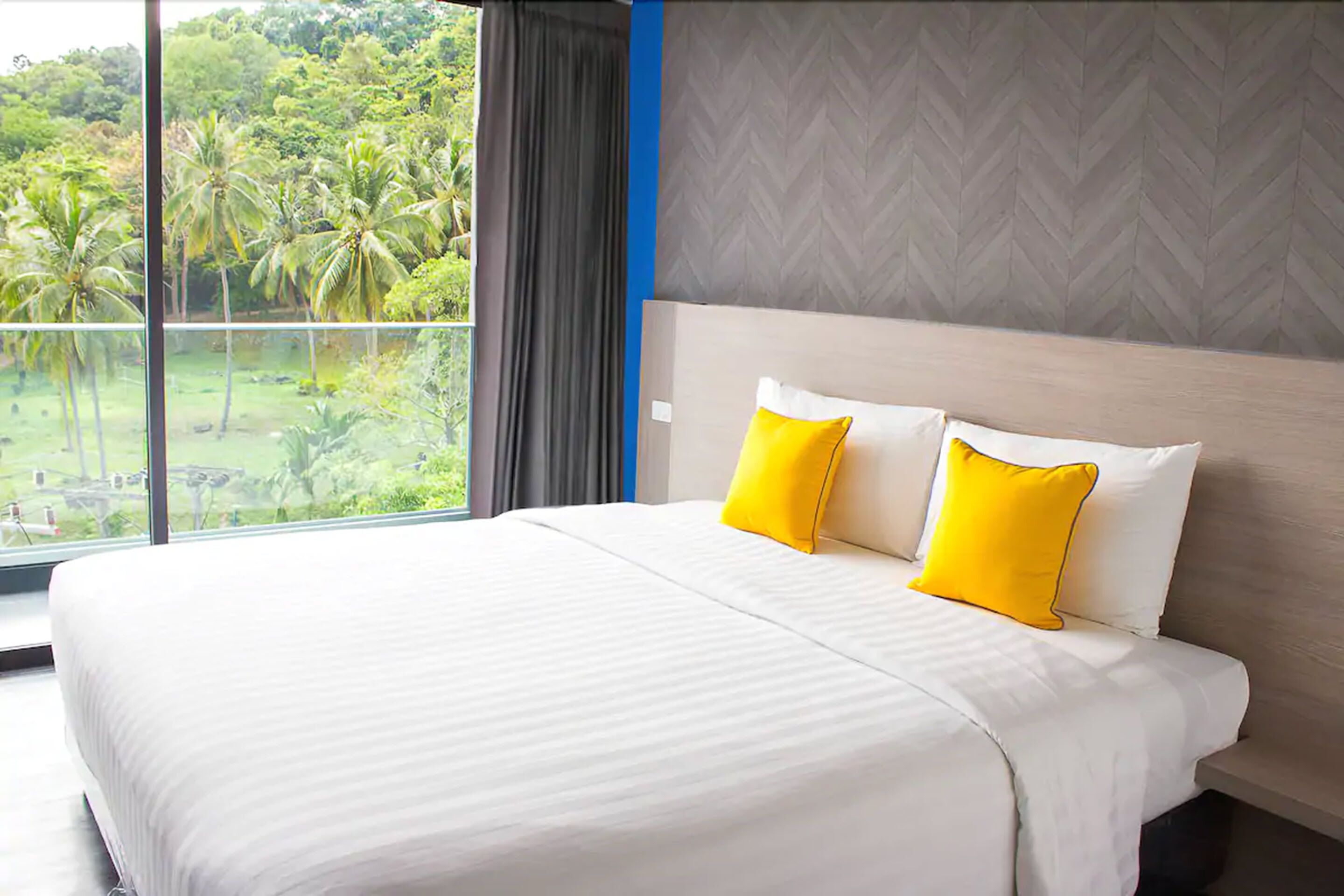 Habitación de hotel con una cama grande, dos almohadas y vistas a zonas verdes, con una pared de diseño en patrón de espiga.