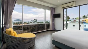 A hotel room with a large window, a bed, a wicker chair with yellow cushions, and an air conditioning unit. - Wake Up Aonang Hotel (Krabi)