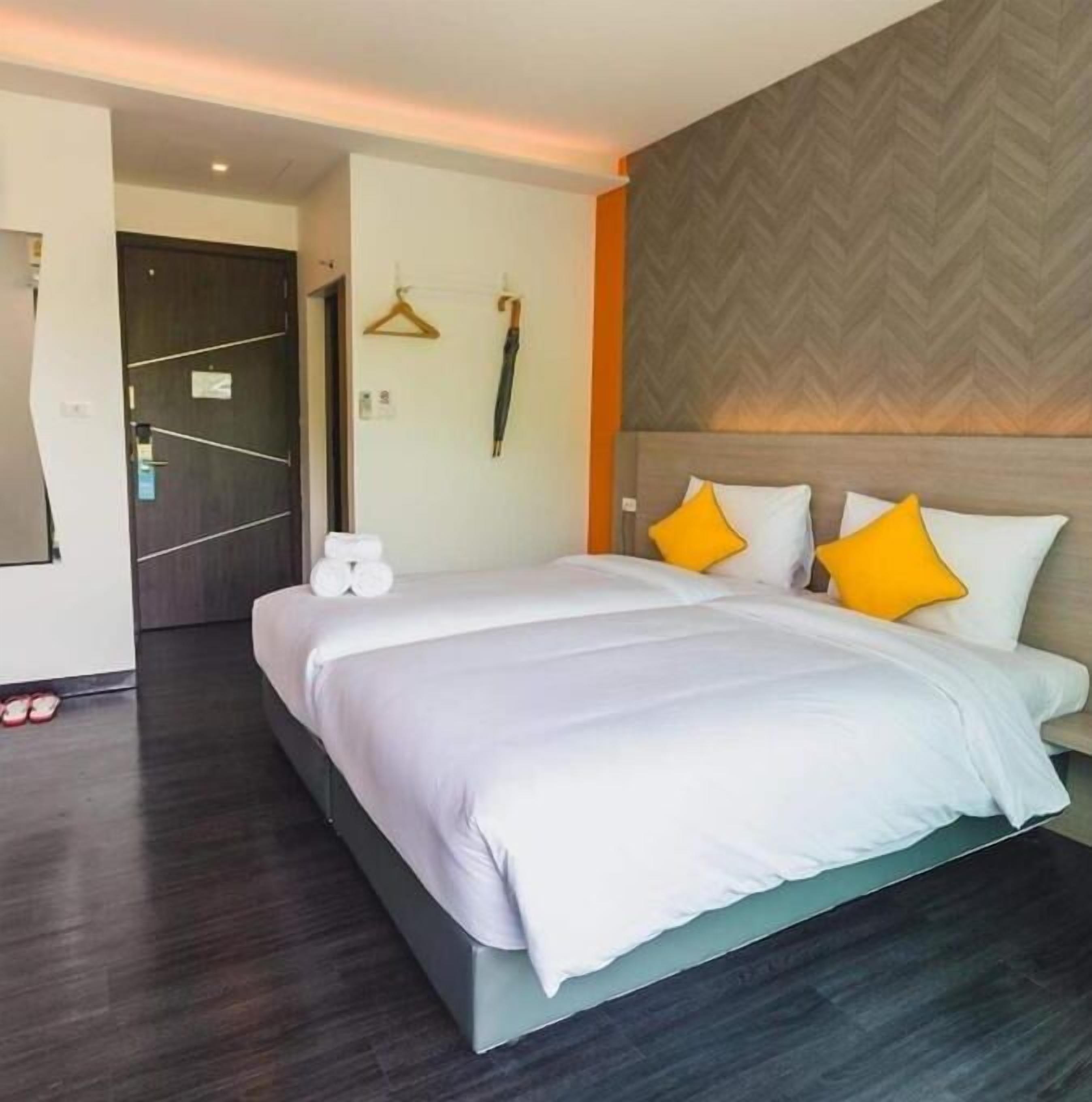 A modern hotel room with a large bed, a wooden headboard, and a herringbone-patterned wall.