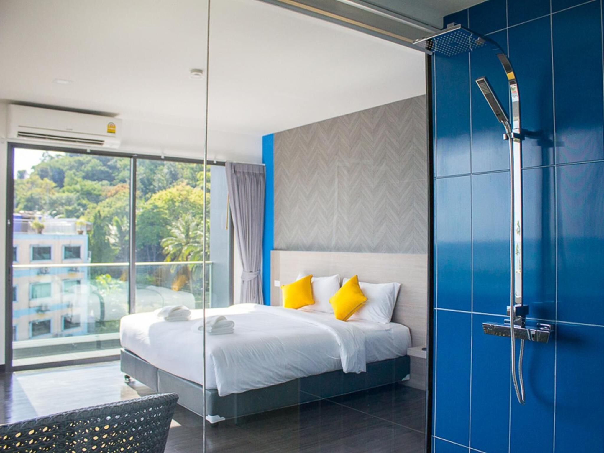 Una habitación de hotel moderna con una cama grande, ducha y balcón con vistas a árboles y edificios.