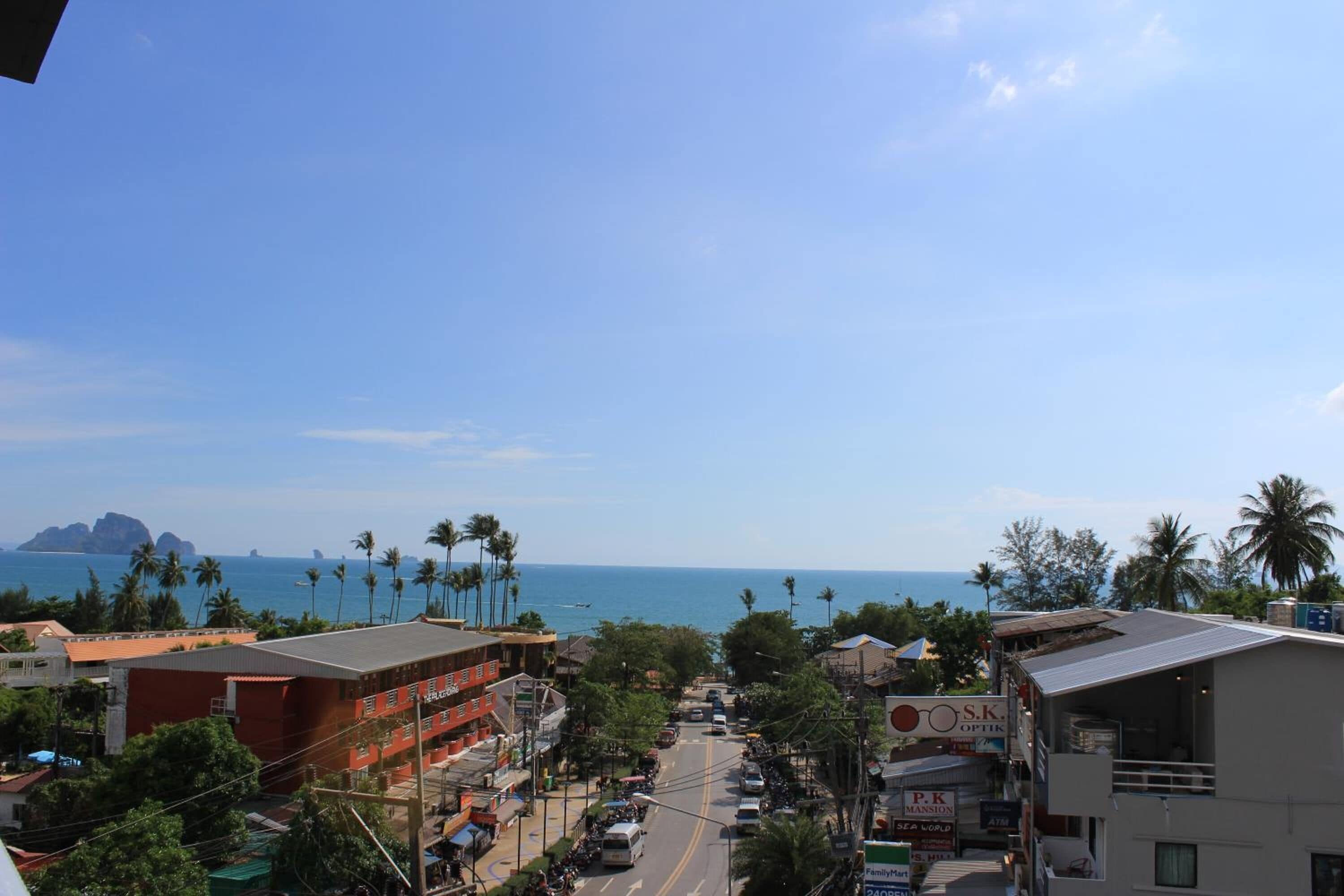 A coastal street with buildings, palm trees, and a view of the ocean.