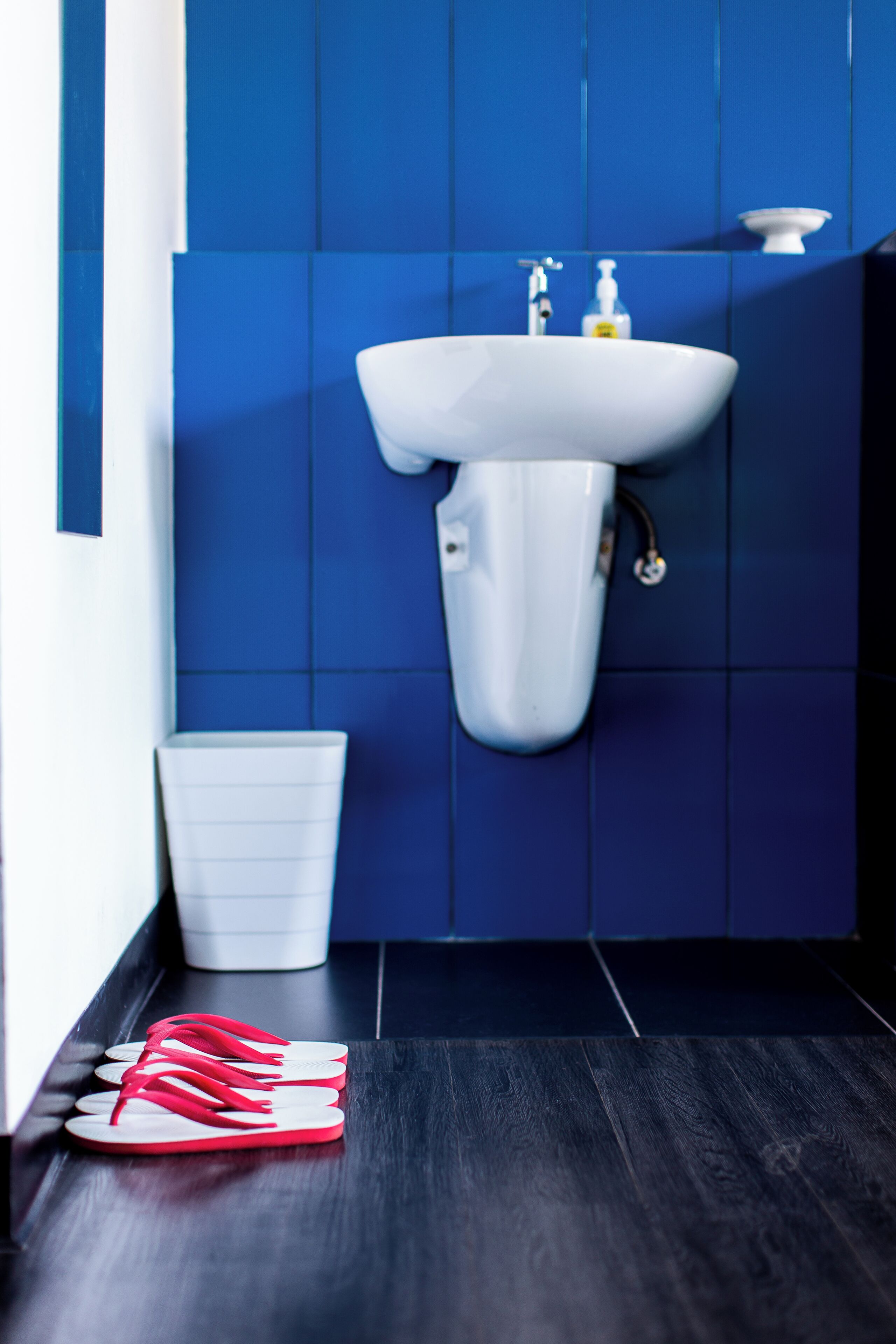 Une salle de bain avec un lavabo blanc, des carreaux bleus et un plancher en bois foncé.