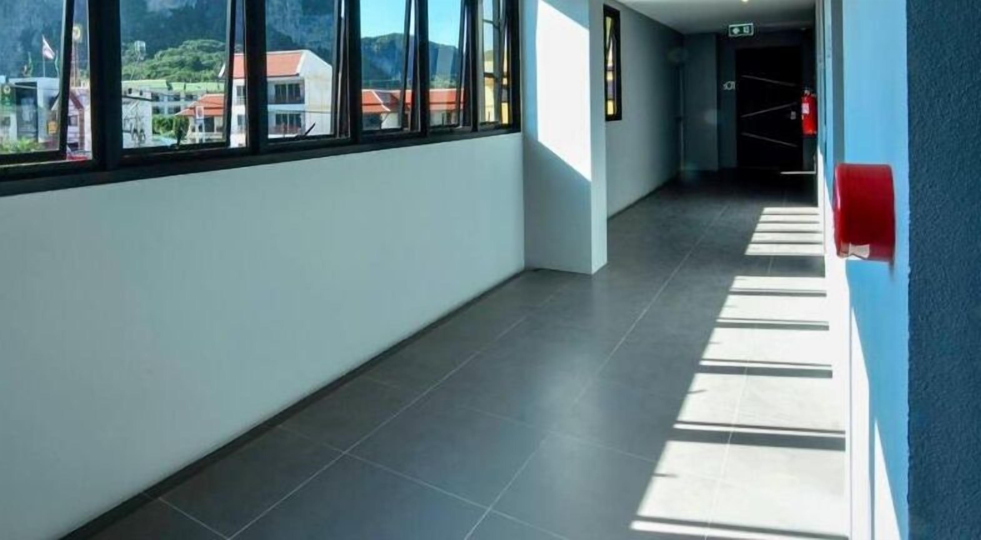 A corridor with large windows, a tiled floor, and a view of buildings in the distance.