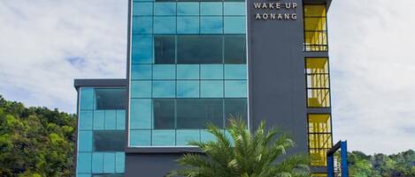 A modern building with a sign reading "WAKE UP AONG" and a palm tree in front.