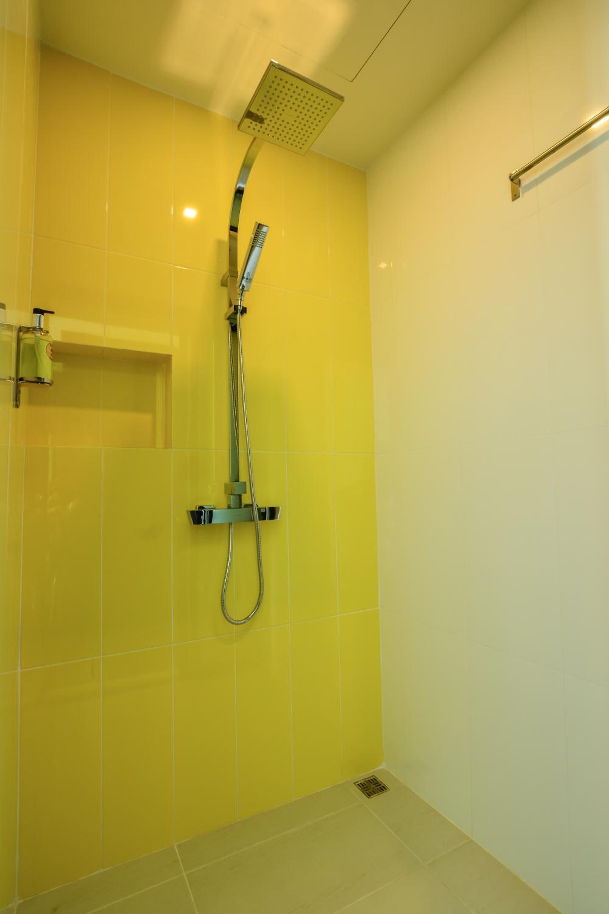 A bathroom with yellow tiles, a showerhead, and a handrail.