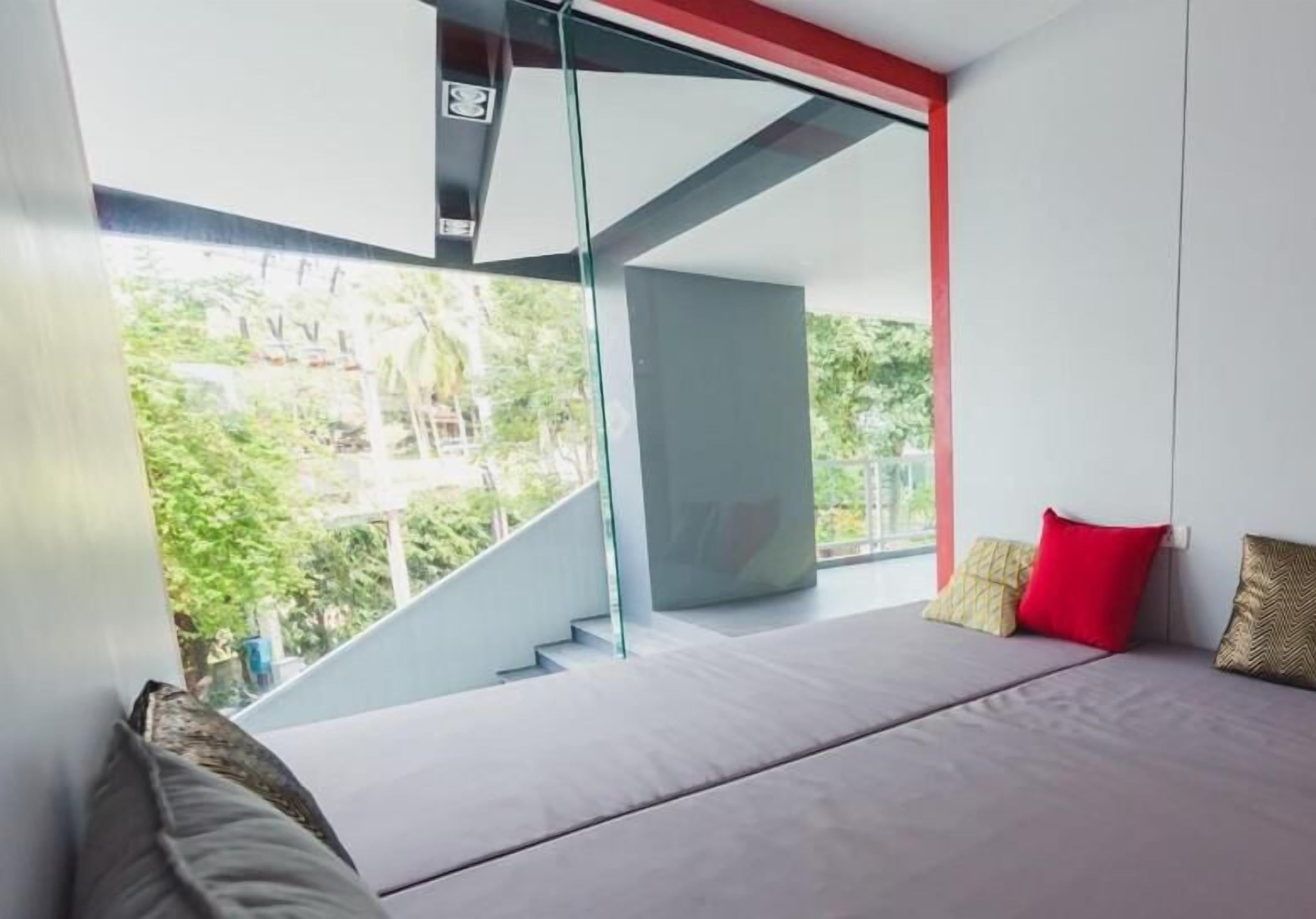 A modern bedroom with a bed, a staircase, and a large window offering a view of greenery outside.