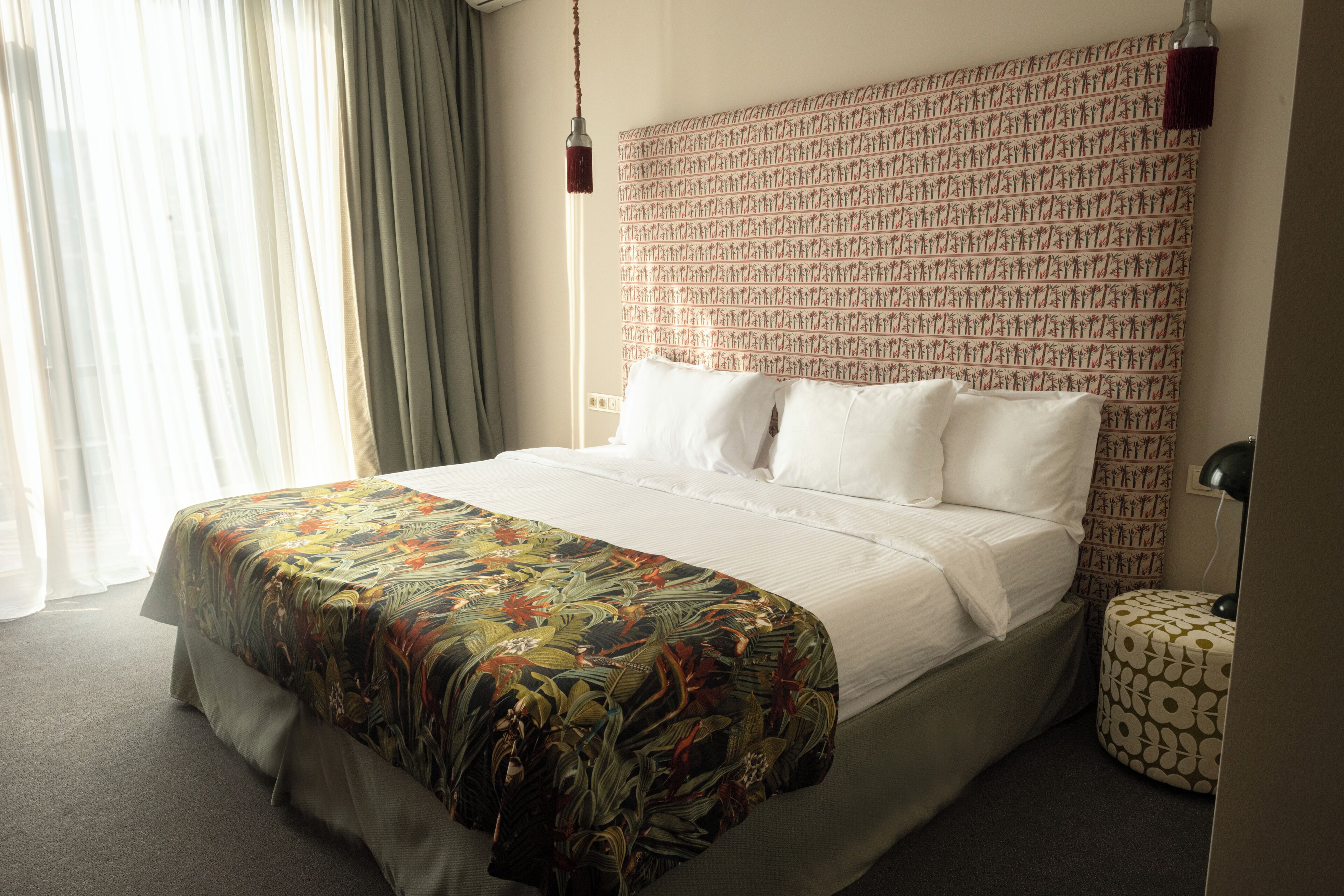 Une chambre d’hôtel avec un grand lit, une tête de lit à motifs et un petit pouf rond.