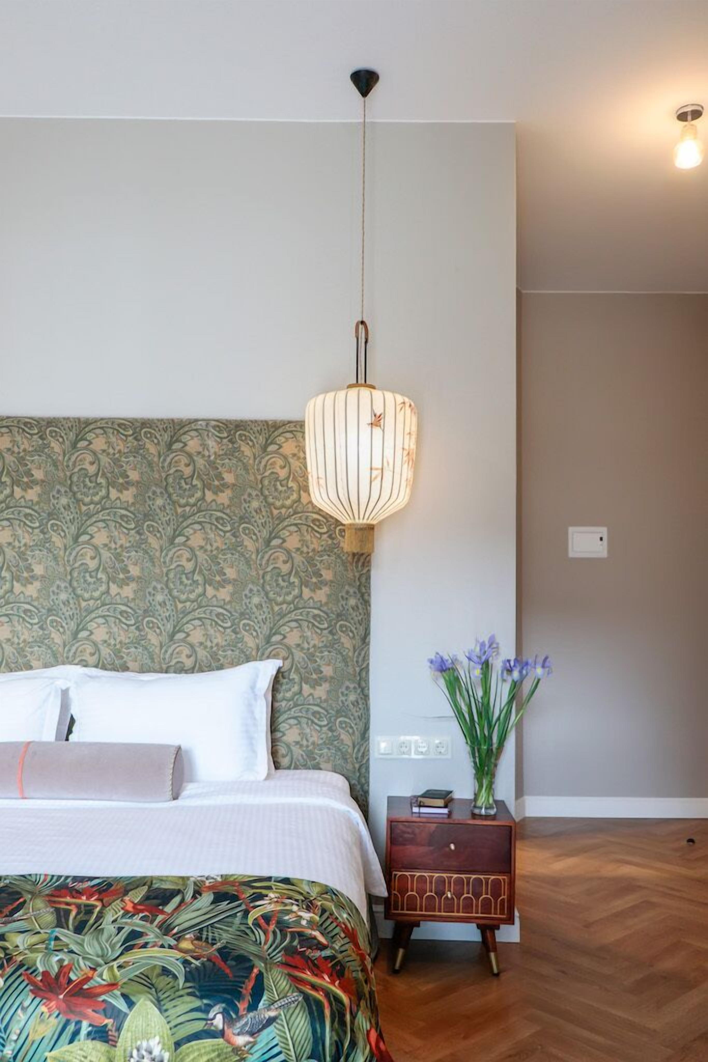 A bedroom with a bed, a nightstand, a decorative lamp, and a wall with a patterned design.